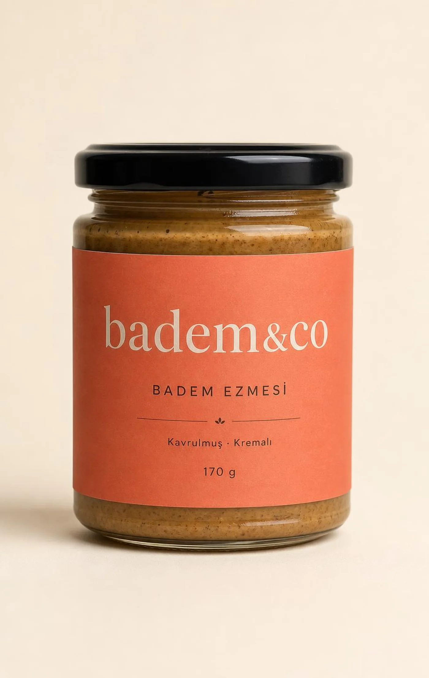 Badem Ezmesi 170 g cam kavanoz, etiketli paketinin ön yüzü: "badem&co" logosu, "BADEM EZMESİ" ürün adı, "Kremsi · Tek malzeme" tanımı ve şekersiz ibaresi ve tek malzeme beyanı