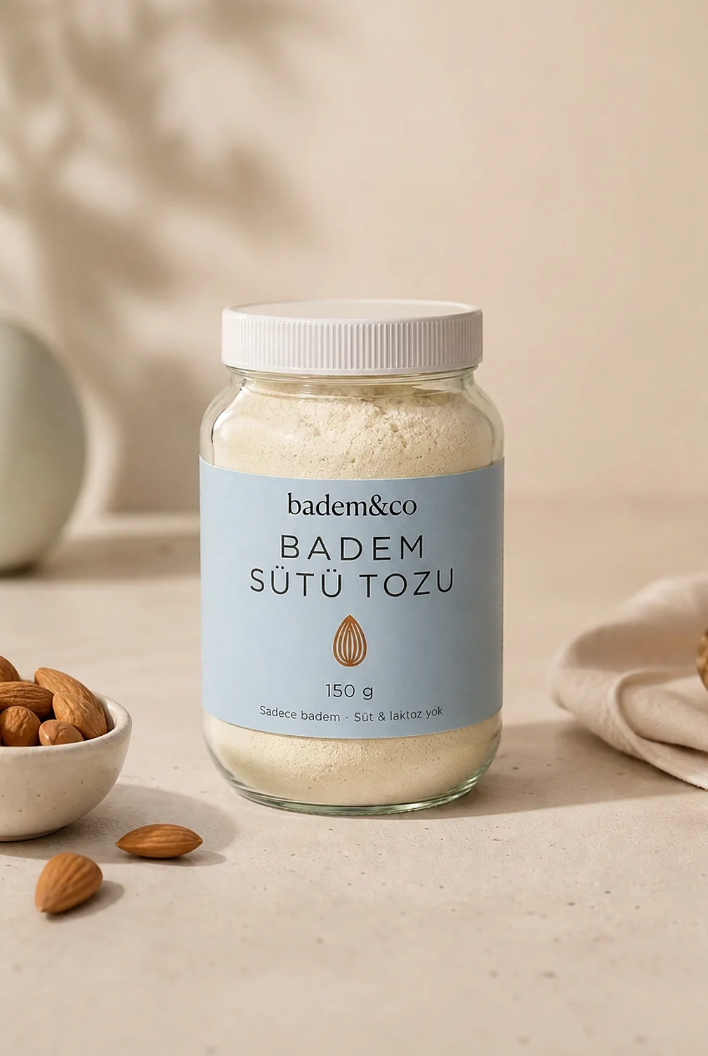 Badem Sütü Tozu 150 g cam kavanoz, etiketli paketinin ön yüzü: "badem&co" logosu, "BADEM SÜTÜ TOZU" ürün adı, "Sadece badem · Süt & laktoz yok" tanımı ve içindekiler ve besin değerleri alanı